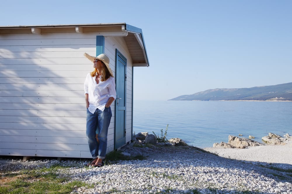 An image of a middle aged woman relaxing next to her white beach house.