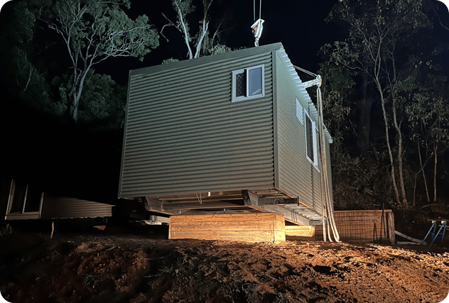 A portable building is being lowered onto the ground by a crane.