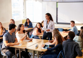 Female,High,School,Teacher,Standing,By,Student,Table,Teaching,Lesson